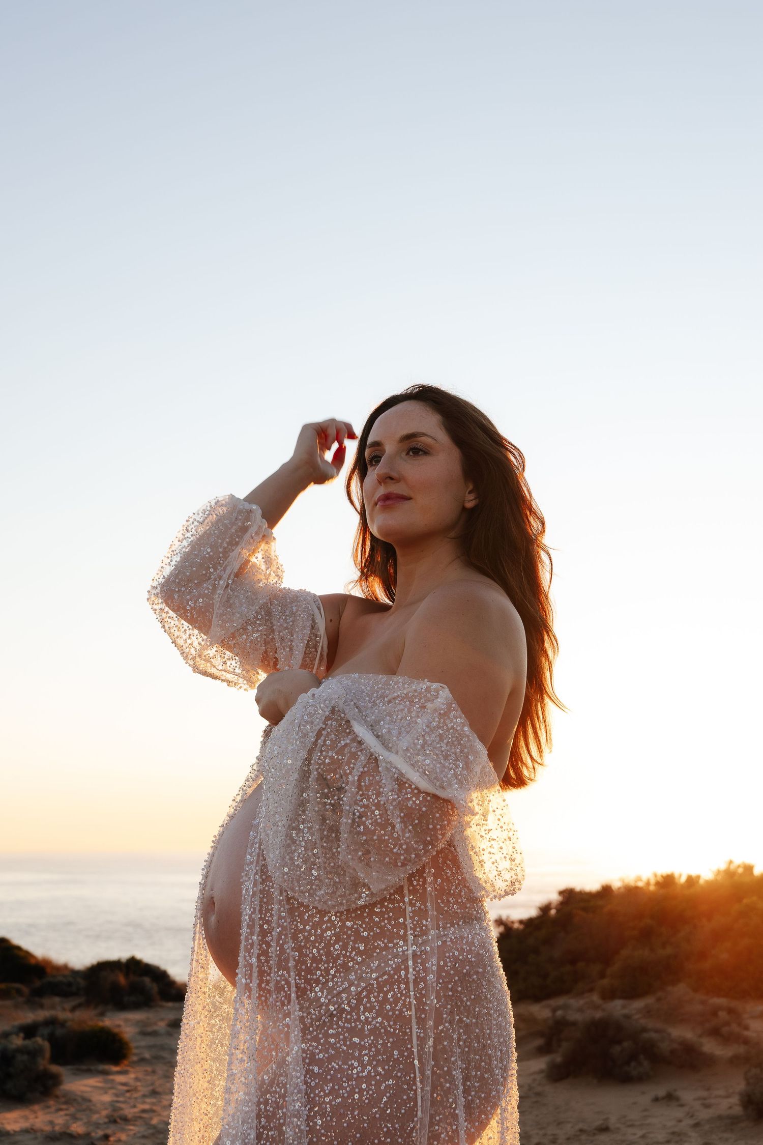 Beach maternity photo in flowing mauve dress during golden hour.
