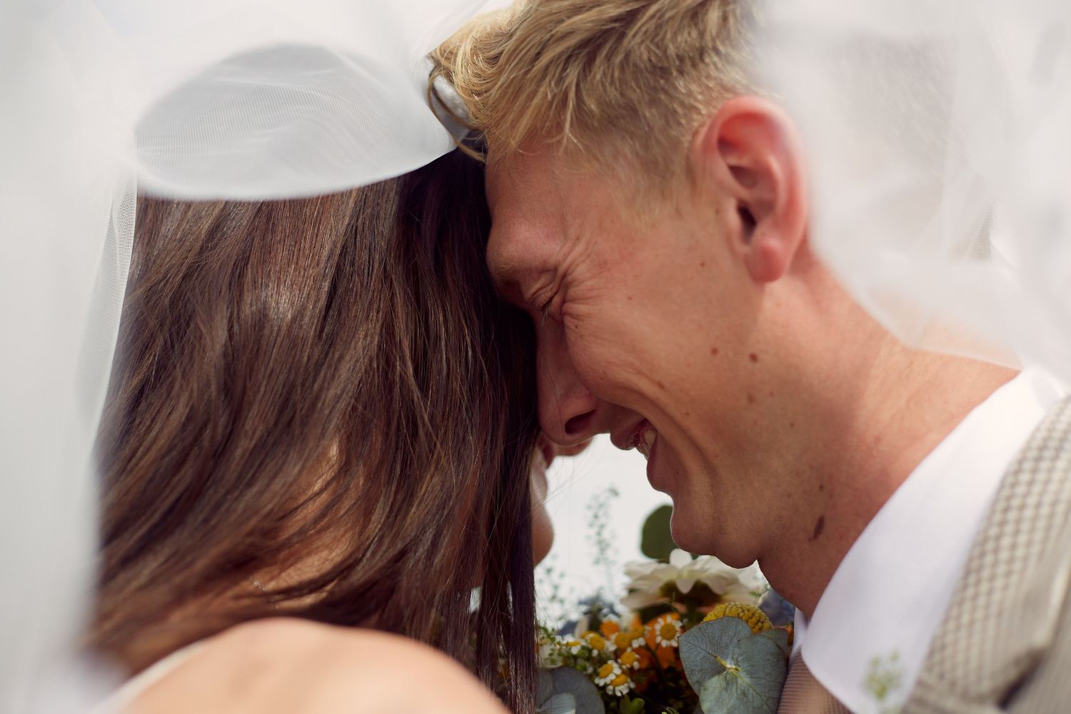 A tender intimate moment between a couple in their wedding attire with white flowers as decor.