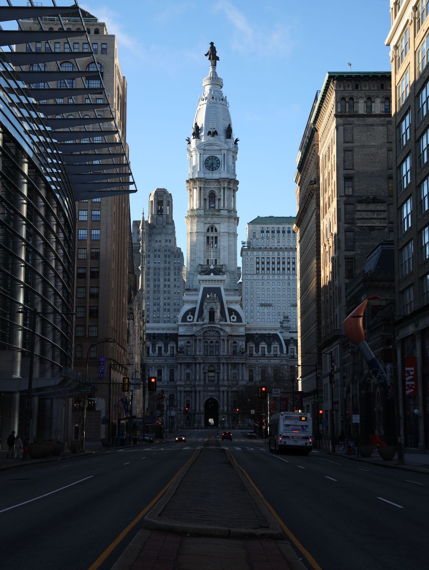 Philadelphia City Hall building with clock tower dominates view down empty street between tall buildings.