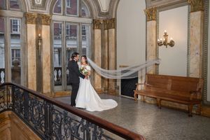A romantic wedding portrait in an elegant historic venue with ornate columns and a flowing veil.