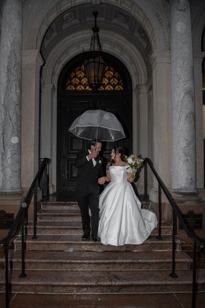 A couple shares a romantic moment under a clear umbrella on rainy stone steps.