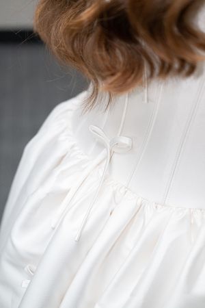 Back view of a white satin dress with delicate ribbon bow detail and gathered fabric on a woman with auburn hair.