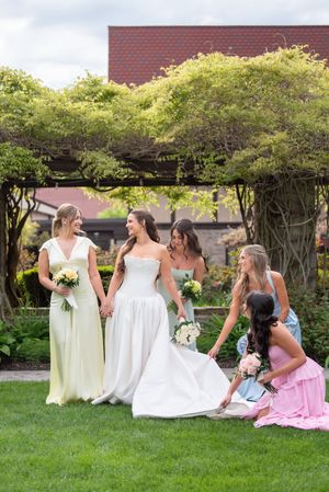 Bride in white gown with bridesmaids in pastel dresses posing outdoors in a lush garden setting.