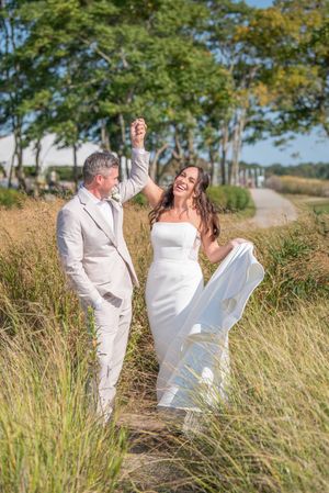 Wedding couple dancing and twirling in tall grass on sunny afternoon.