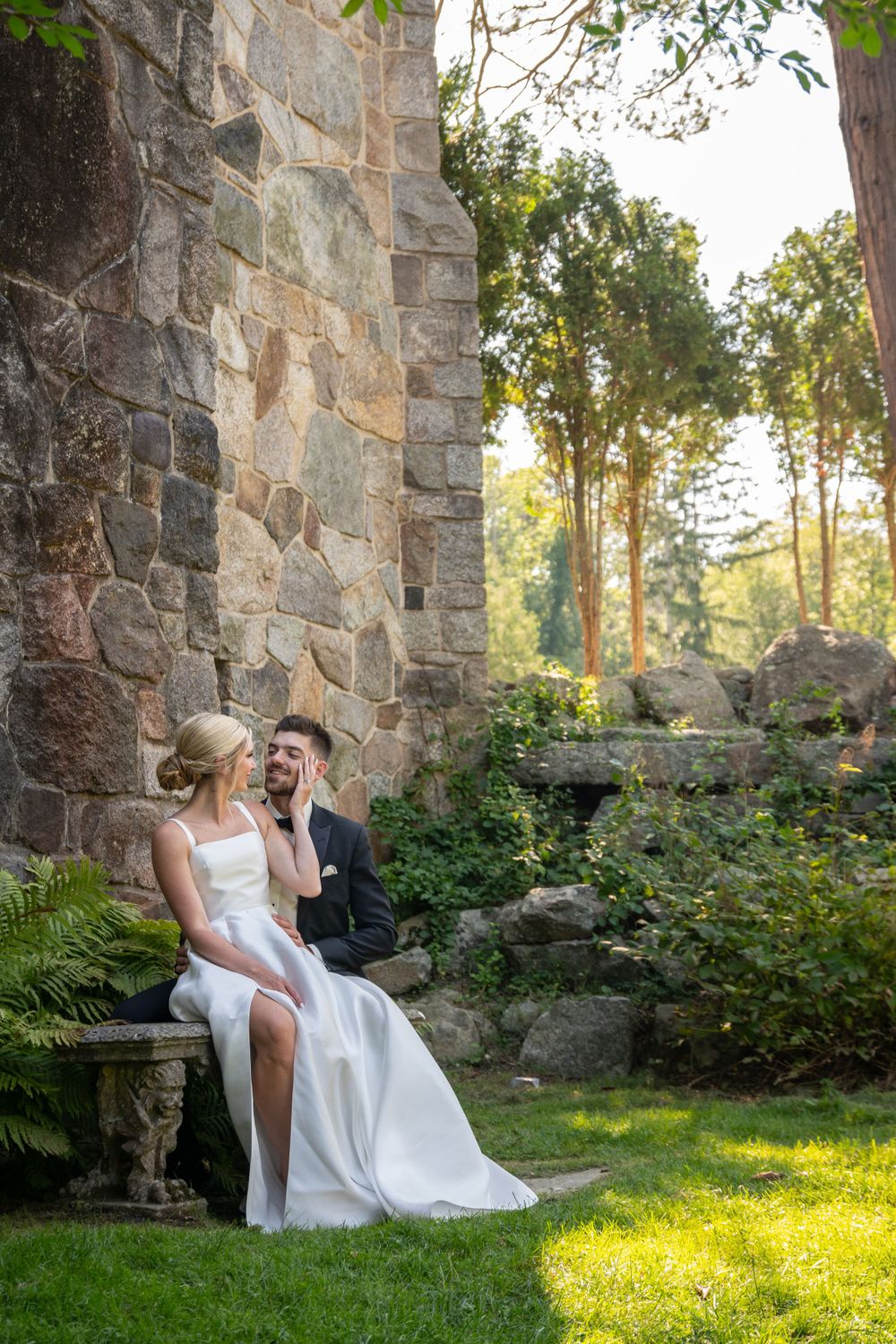 A romantic scene by a stone wall with sunlight filtering through trees.