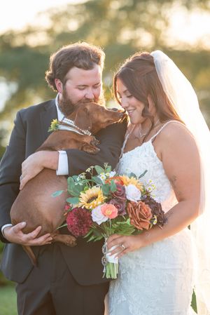A couple shares intimate kisses while holding a vibrant autumn-colored wedding bouquet.