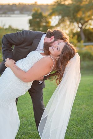 A romantic wedding couple shares a dramatic dip kiss in a sunlit outdoor setting.