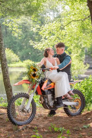 A unique wedding photo featuring a dirt bike in a lush forest setting with sunflowers.