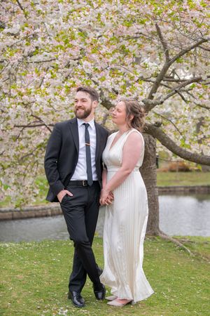 A joyful moment captured under blooming cherry blossoms beside a pond in springtime.