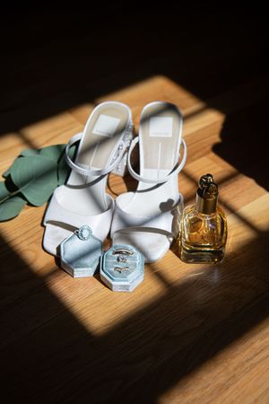 White bridal shoes and perfume bottles arranged artistically in sunlight on wooden surface.
