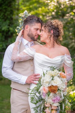 Romantic wedding couple embracing outdoors with white floral bouquet in garden setting.