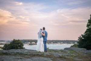 A scenic coastal wedding portrait with distant water views and soft clouds.