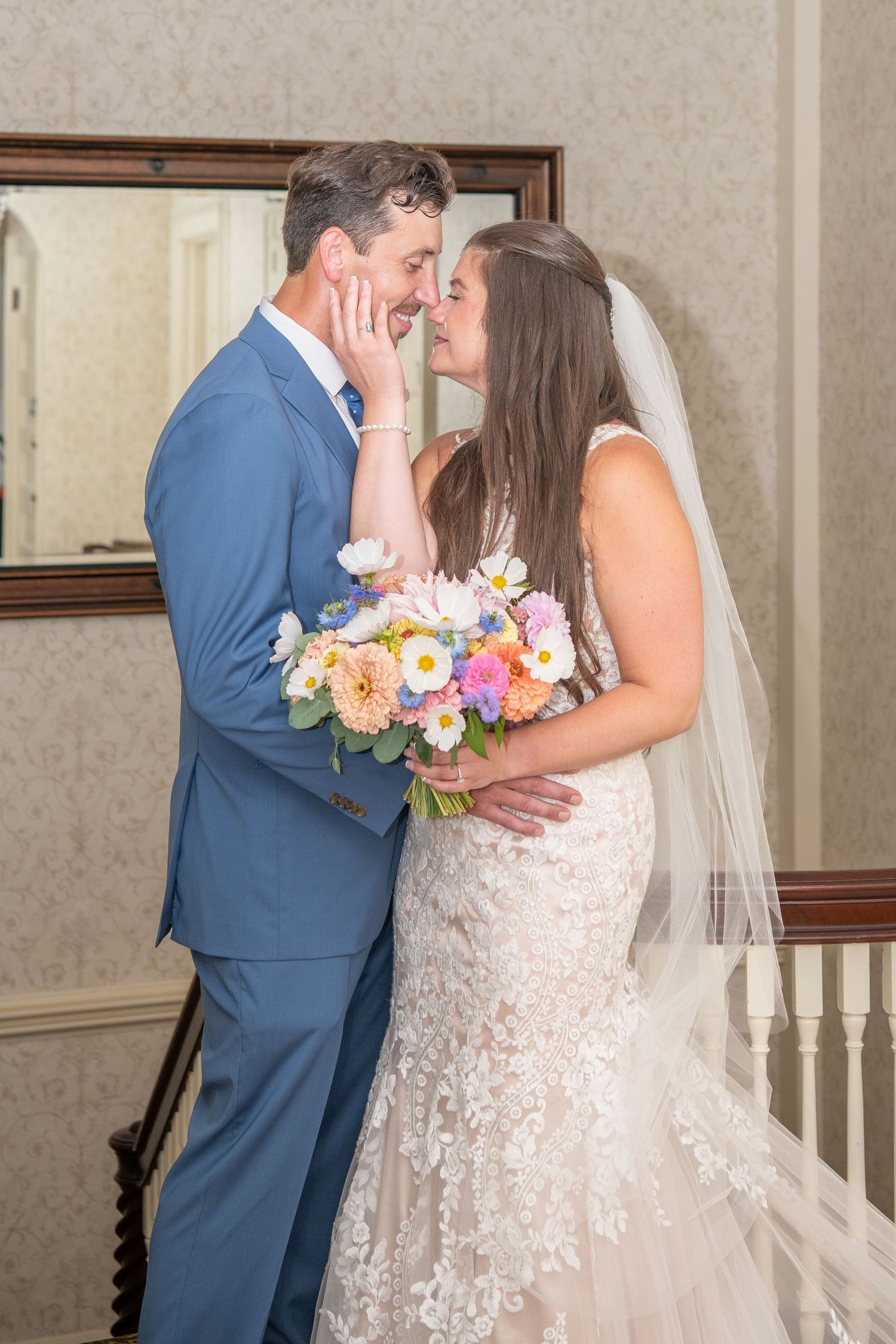 A tender wedding moment captured indoors with colorful floral bouquet and lace details.