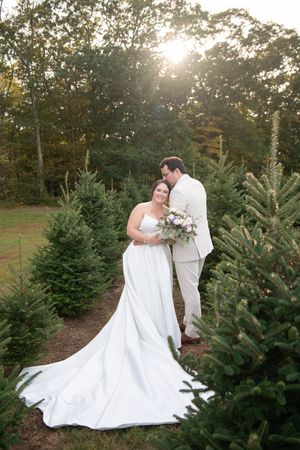 A romantic wedding photo session among evergreen trees at sunset with a flowing white dress and soft lighting.