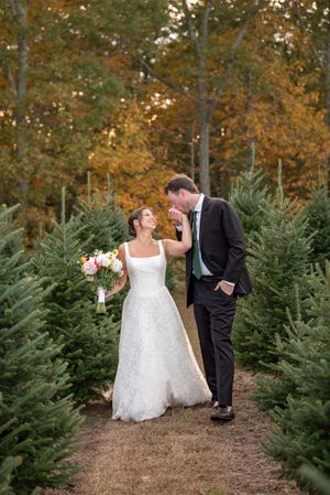 A romantic wedding moment captured among evergreen trees with autumn foliage in the background.
