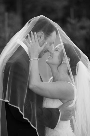 A romantic black and white photo of a couple sharing an intimate moment under a wedding veil.