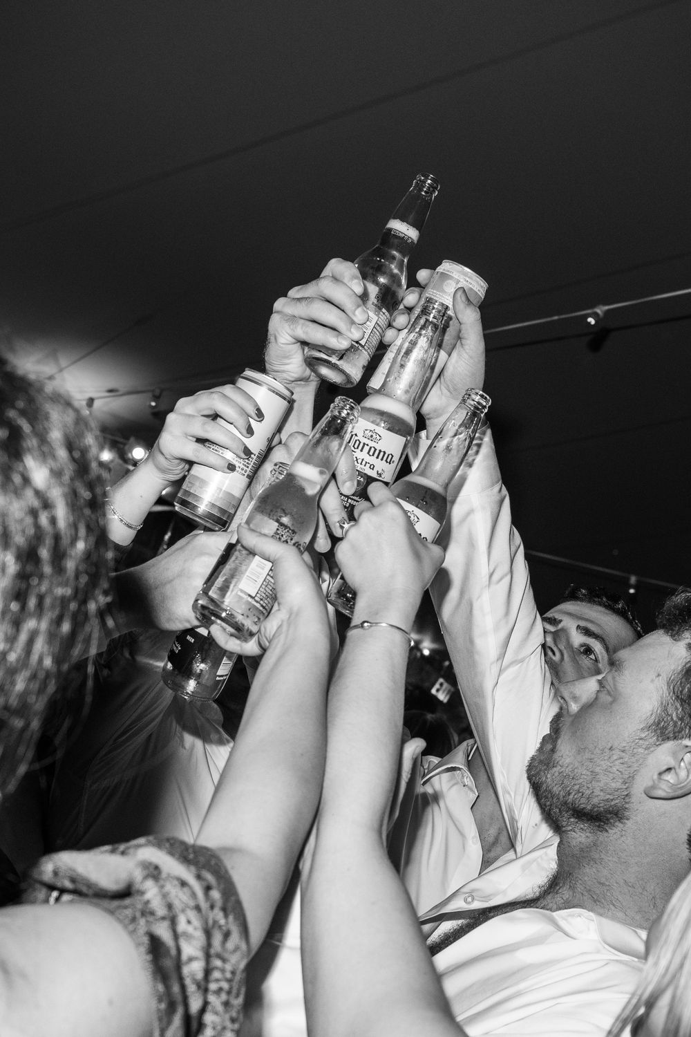 Black and white image of guests toasting with bottles raised high during wedding celebration.