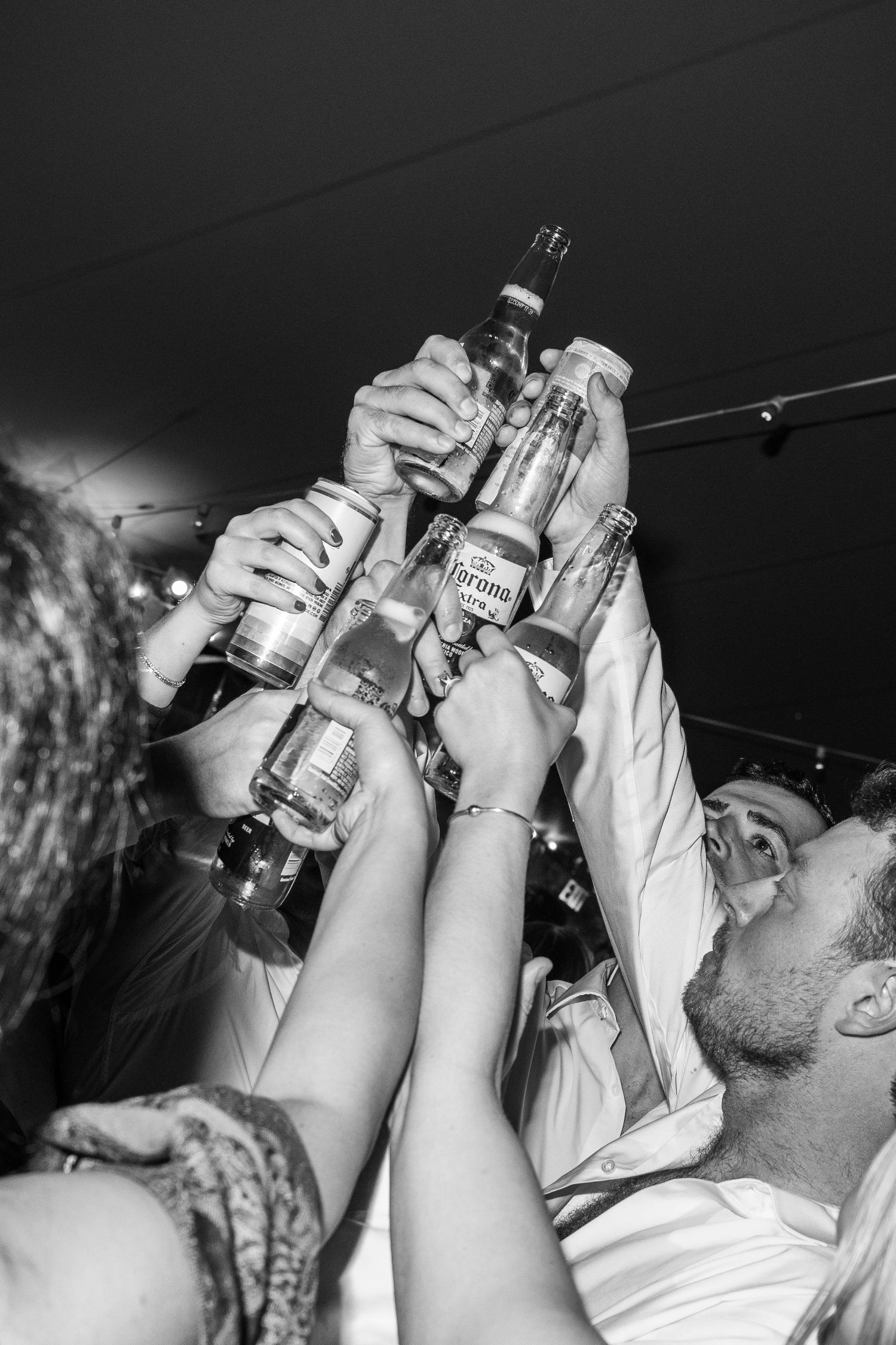 Black and white image of guests toasting with bottles raised high during wedding celebration.