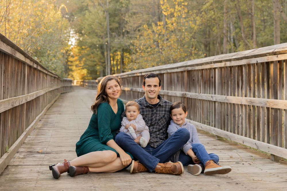 family sitting on a boardwalk smiling for a photo in an Oakland county michigan park