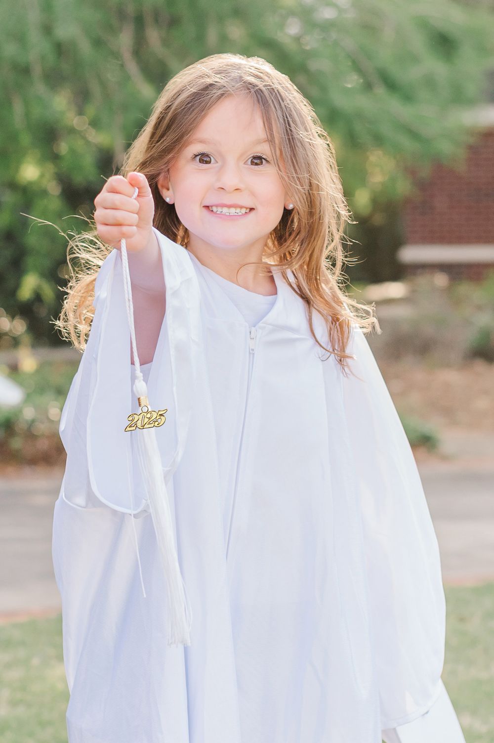 Kindergarten graduate in white 2025 tassel posing with a greenery background, Newnan, GA