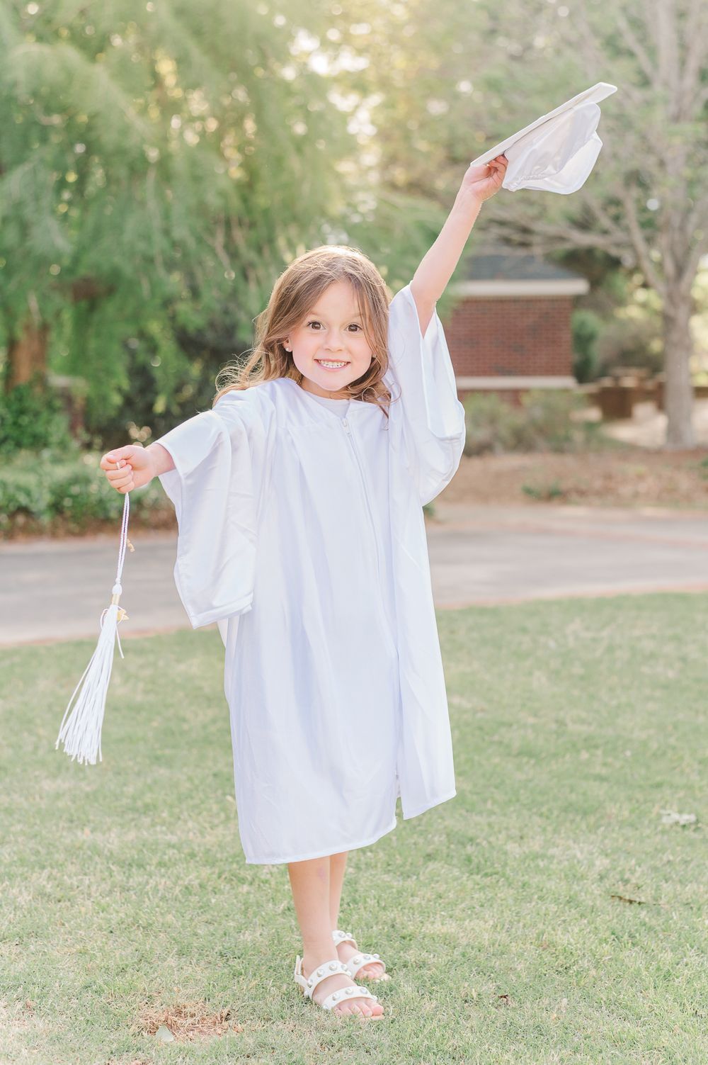 Kindergarten graduate in white cap and gown posing with a greenery background, Newnan, GA