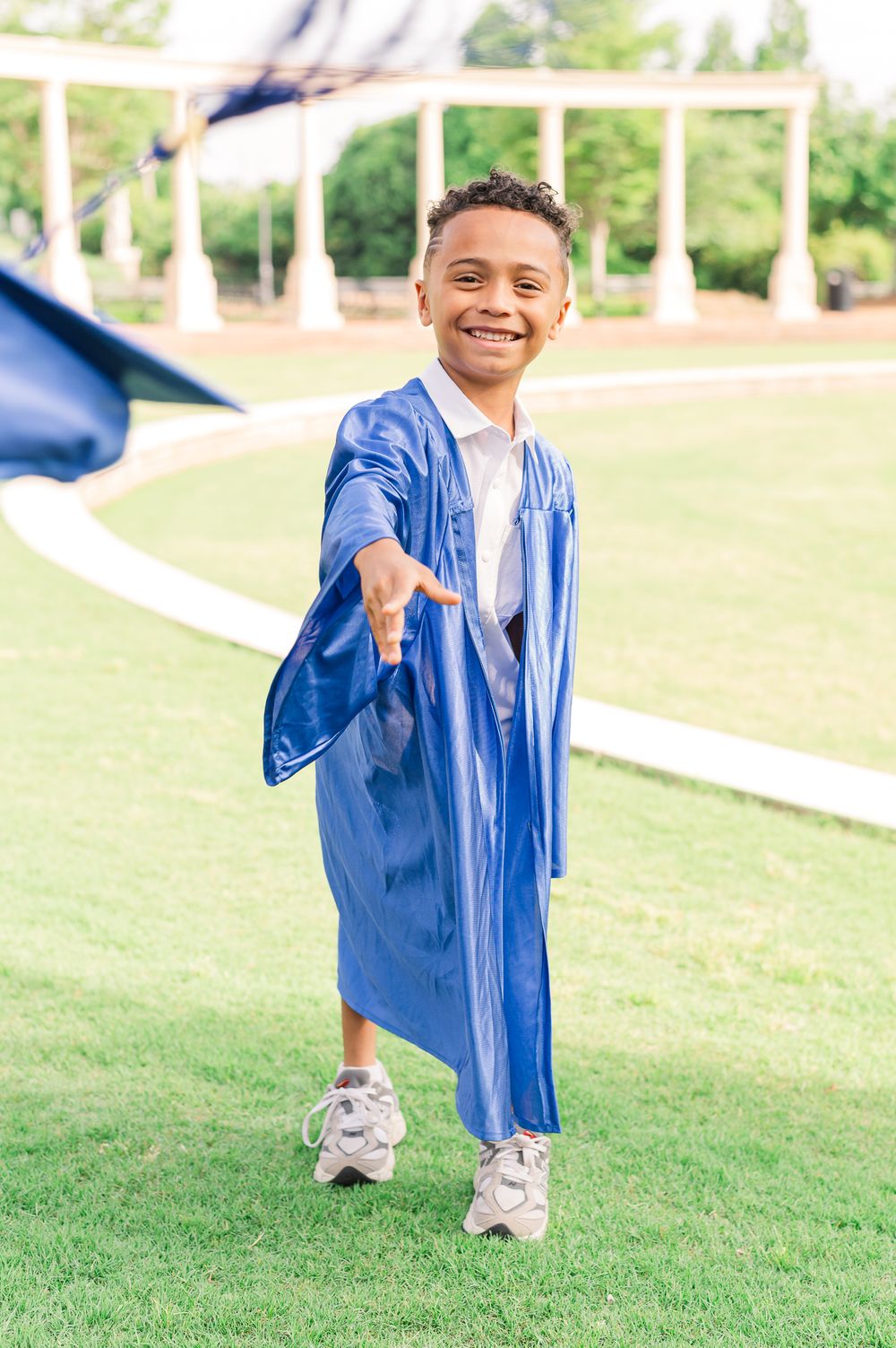 Kindergarten grad in blue cap and gown throwing cap, Newnan, GA
