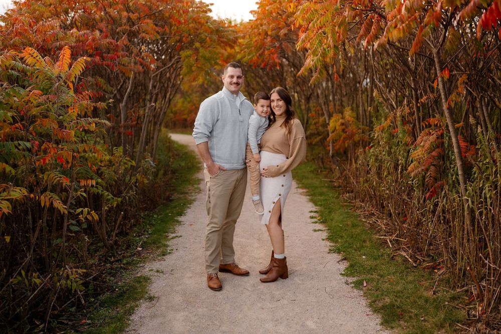 A couple walks hand in hand down a path surrounded by vibrant autumn foliage in warm orange and red hues.