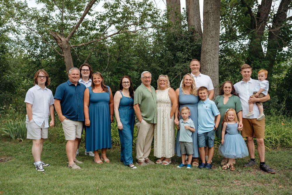A large family group poses together outdoors in coordinated blue and neutral colored outfits on a summer day.
