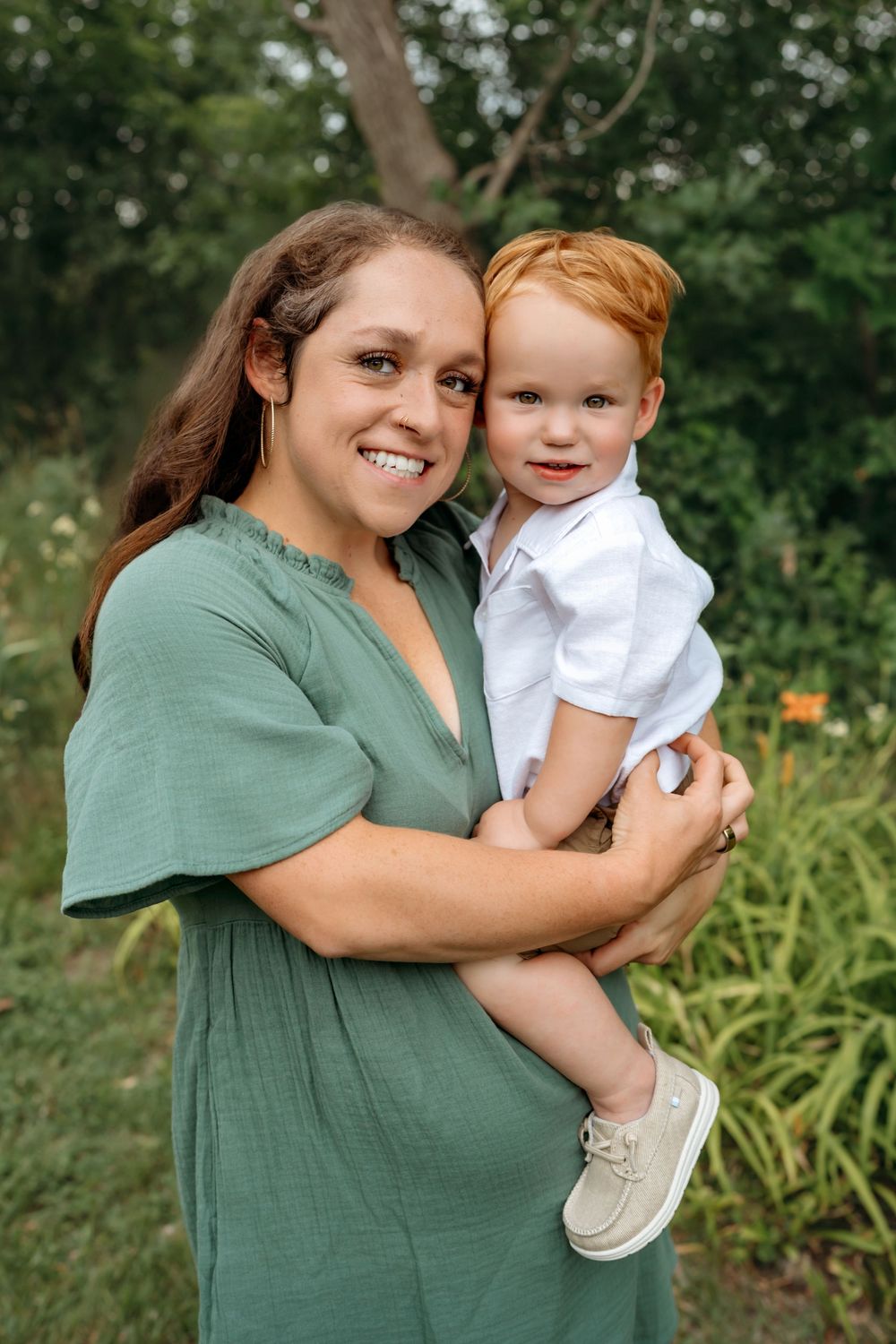 A loving portrait in a garden setting shows a parent in green dress holding a small child in white shirt.