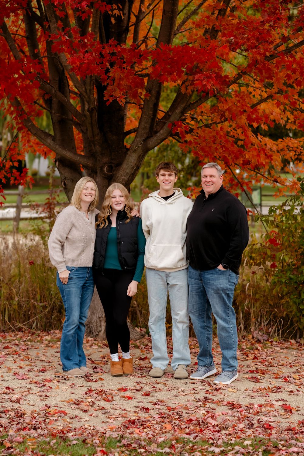 A group stands together under a vibrant red maple tree in autumn with fallen leaves scattered on the ground.