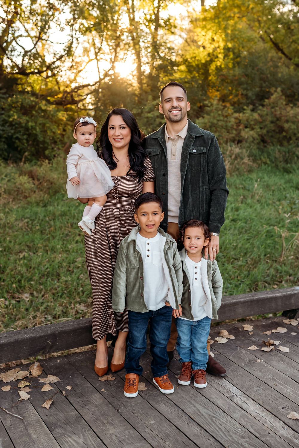 Family poses together on wooden deck during golden hour sunset in autumn setting.