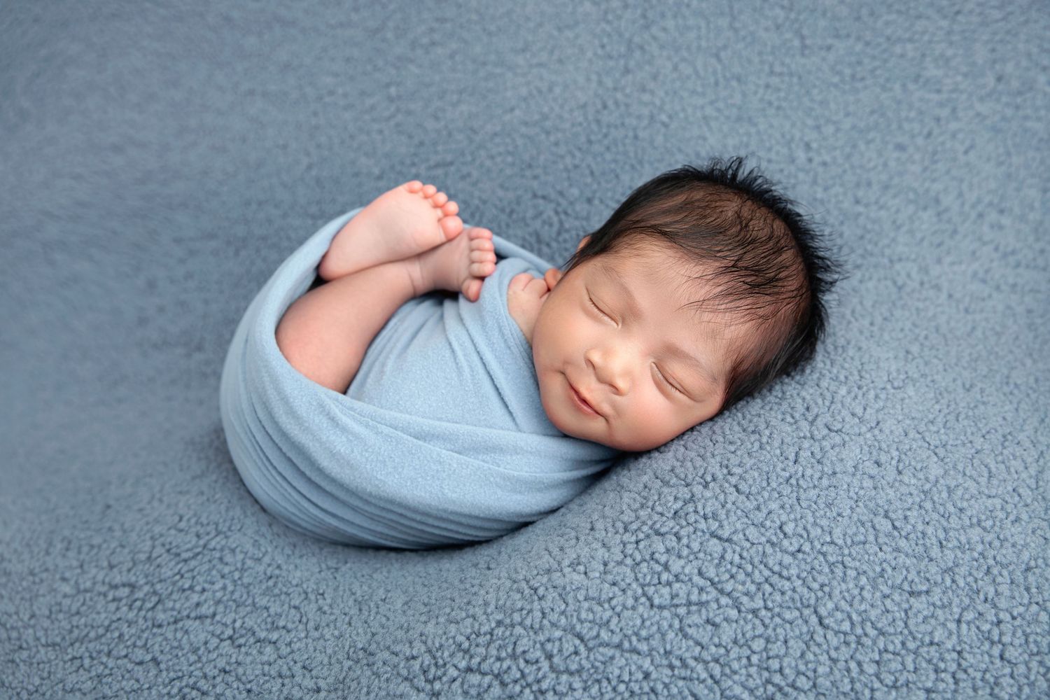Peaceful newborn wearing delicate floral crown sleeps wrapped in cream fabric.