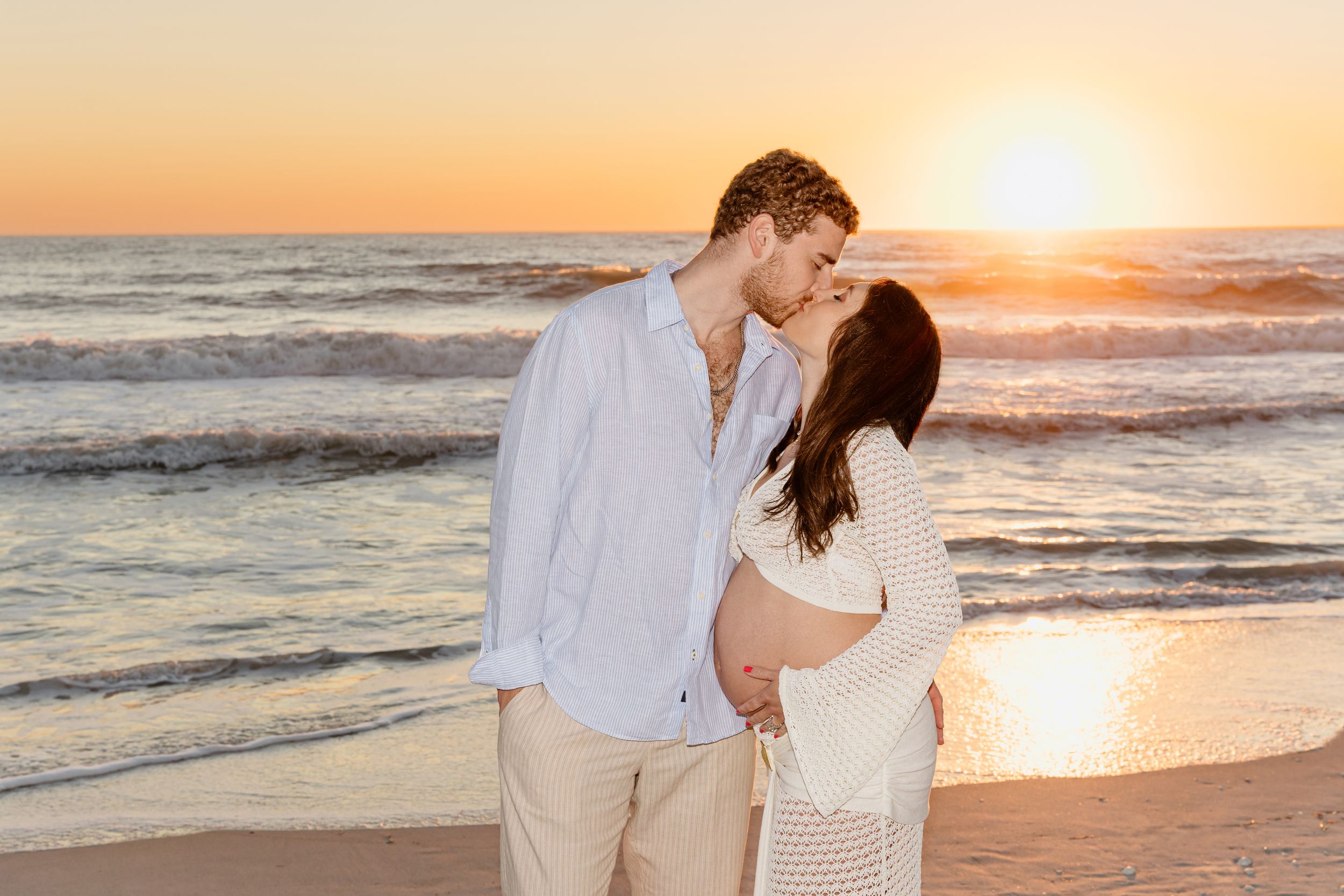 A romantic couple shares tender moments on the beach during a golden sunset photoshoot.