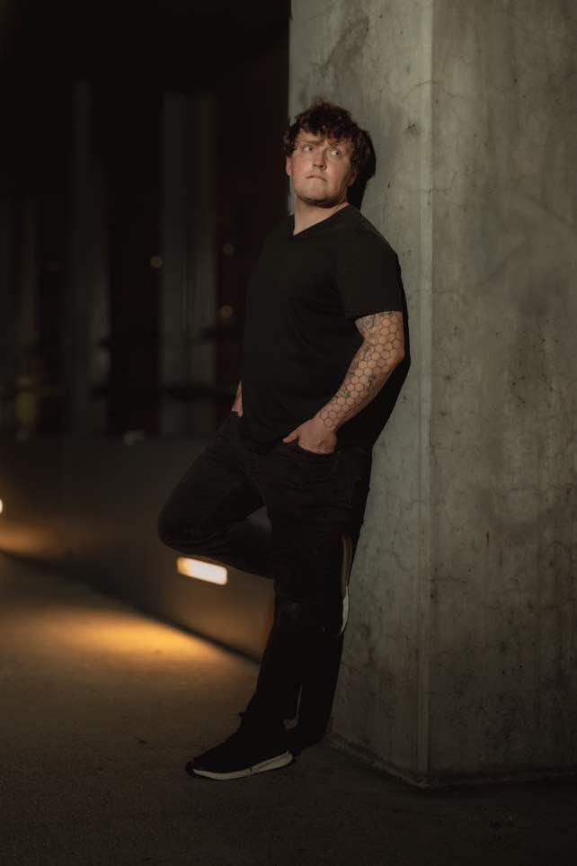 Dramatic low-light portrait against concrete pillar in dark urban setting.