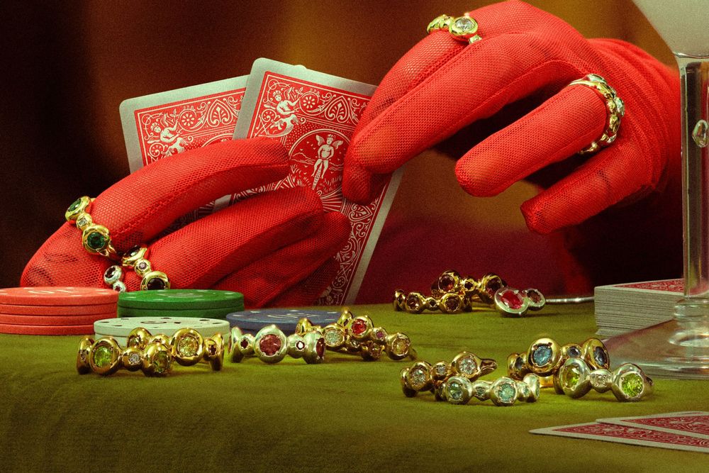 Red gloved hands with jewelry display playing cards and necklaces on a green velvet surface.