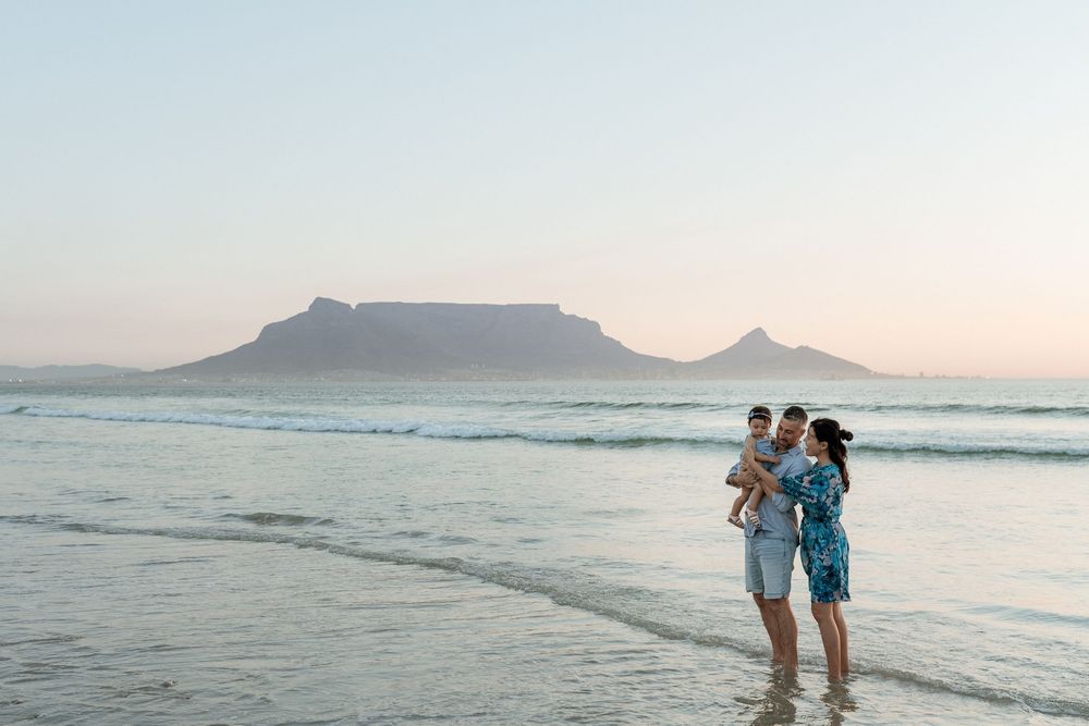 Family standing on a beach with Table Mountain backdrop at sunset in Cape Town, South Africa.