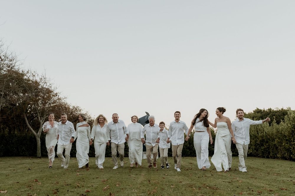 Group of people in white outfits jumping in formation outdoors against natural landscape background.