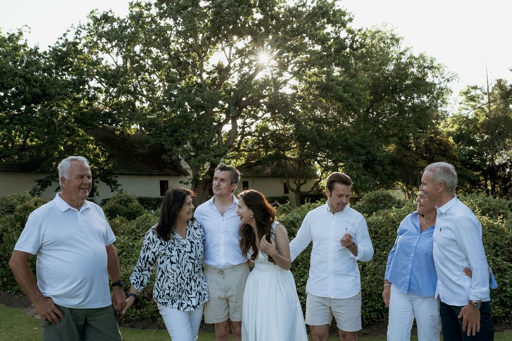A group of people enjoying conversation and laughter together outdoors at sunset in a garden setting.