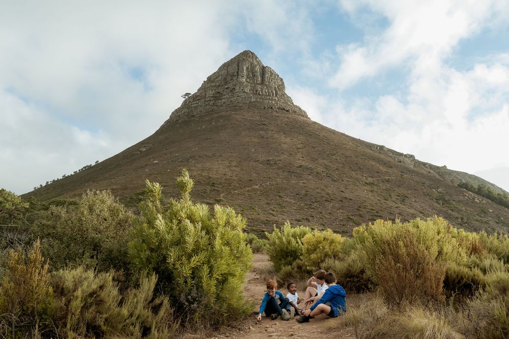 Hikers resting on a trail surrounded by fynbos shrubs at the base of Lion's Head mountain in Cape Town.