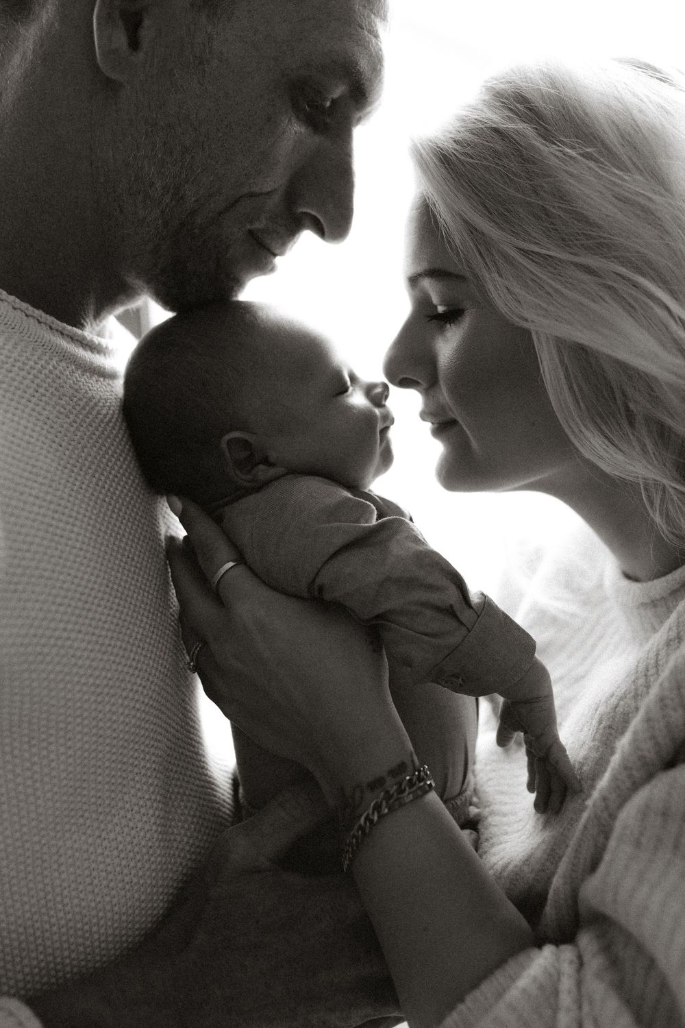 Black and white photo of parents lovingly holding their newborn baby close together.