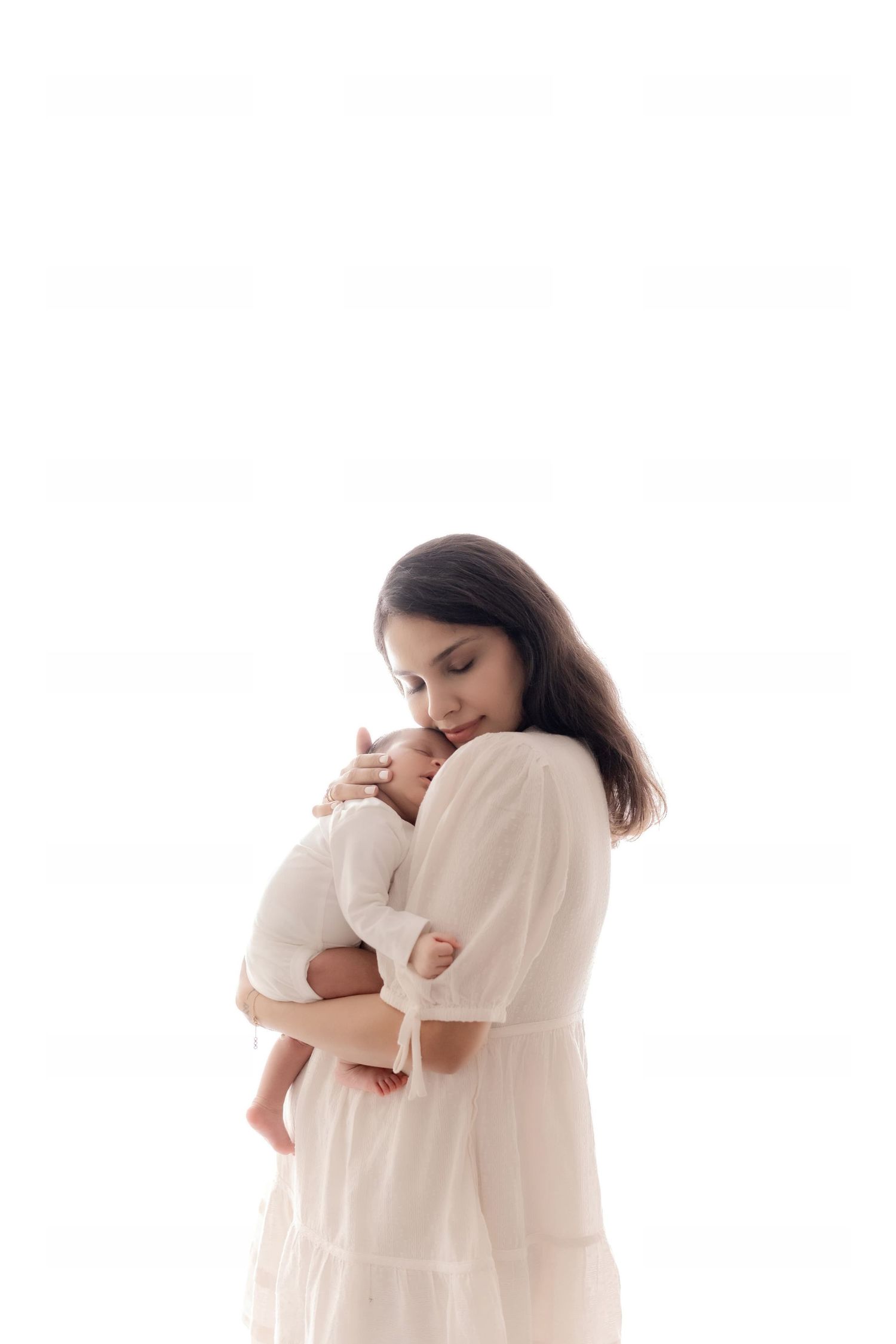 A tender moment between parent and baby dressed in soft white against a plain background.