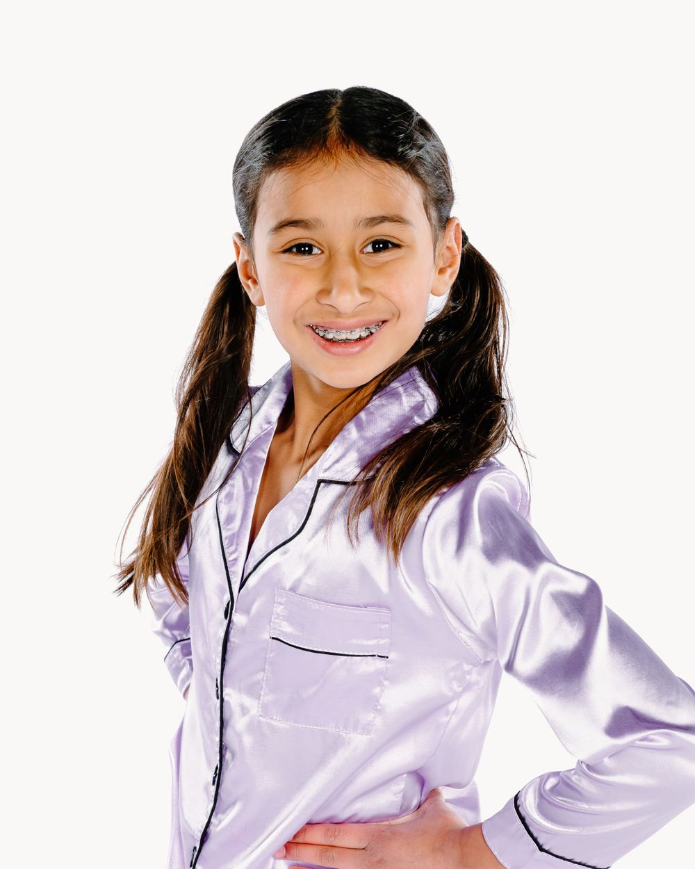 Young person wearing light purple satin pajama top with pigtails smiles cheerfully against white background.