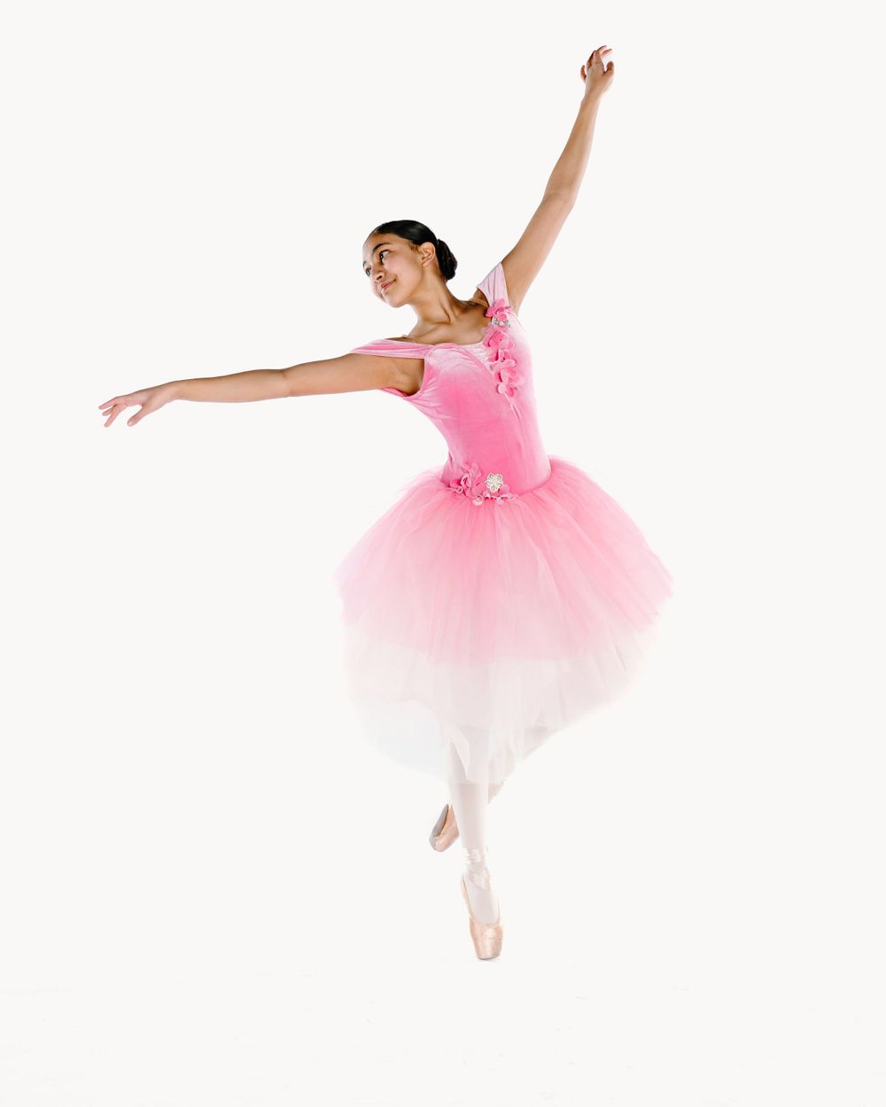 Ballet dancer in pink tulle tutu performs graceful leap against white background.