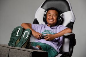 A young person relaxes in a gaming chair wearing headphones with green-soled sneakers propped up to show the number 10.