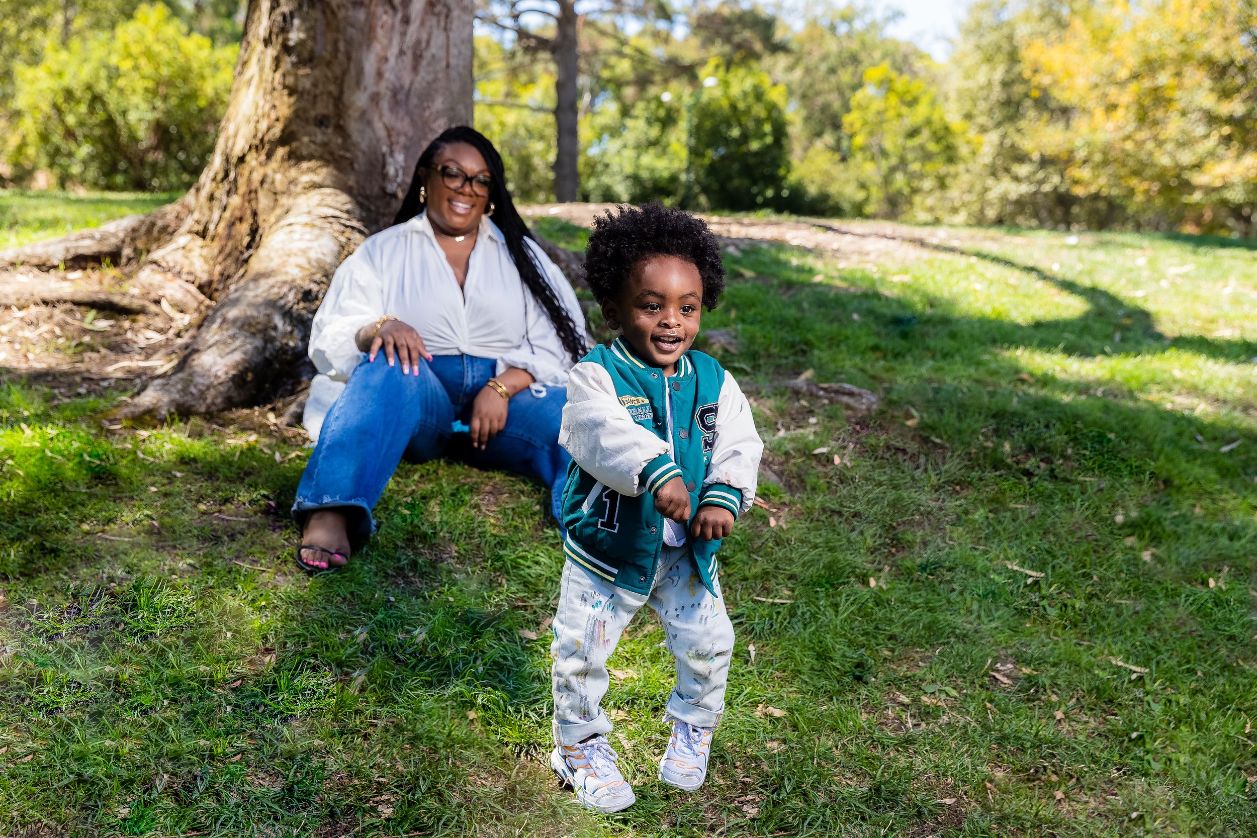 A child plays joyfully in a park while an adult relaxes nearby on a sunny autumn day.