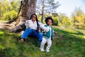 Two people relax outdoors on a grassy hill by a tree trunk on a sunny autumn day.