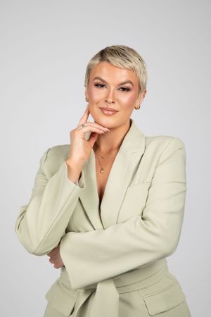 Professional studio portrait of a person in a light beige blazer posing thoughtfully against a gray background.