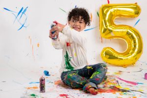 Colorful paint splattered on floor and wall during fifth birthday celebration with gold balloon number decoration.