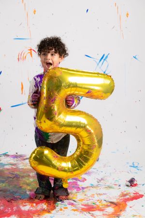 A gold metallic number 5 balloon stands out against a white background with colorful paint splatters and decorative accents. Birthday photos