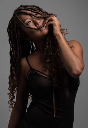 Artistic portrait in black and white style features long dreadlocks and a black tank top against dark background.
